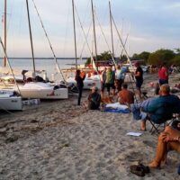 sailboats, including a Beneteau First 18 SE sailboat, pulled up on beach with people sitting in chairs and congregating