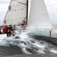 group of men sailing a Beneteau First 27 SE over a wave