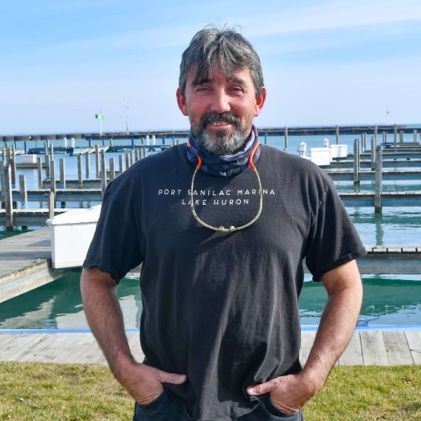 Service Technician Steve Beaudett, a smiling man with salt and pepper hair standing in front of Port Sanilac Marina docks