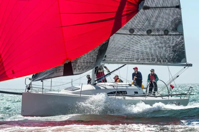 J-Boat J/111 sailboat maned by a crew of six with large red and black sails.