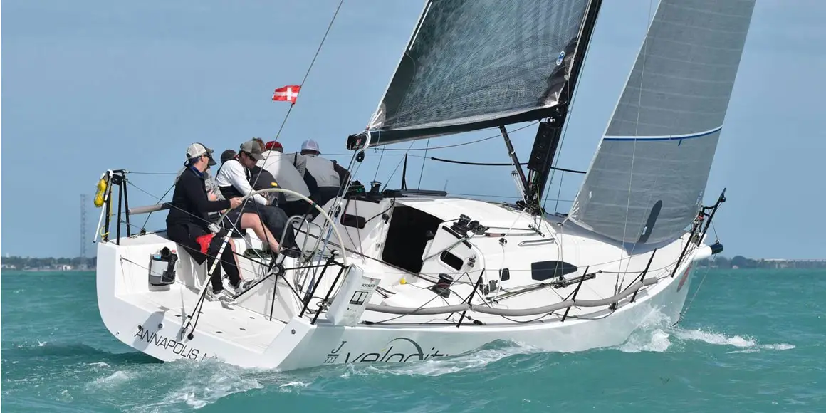 Large crew manning a J-Boat J/111 sailboat titling sharply in the water.