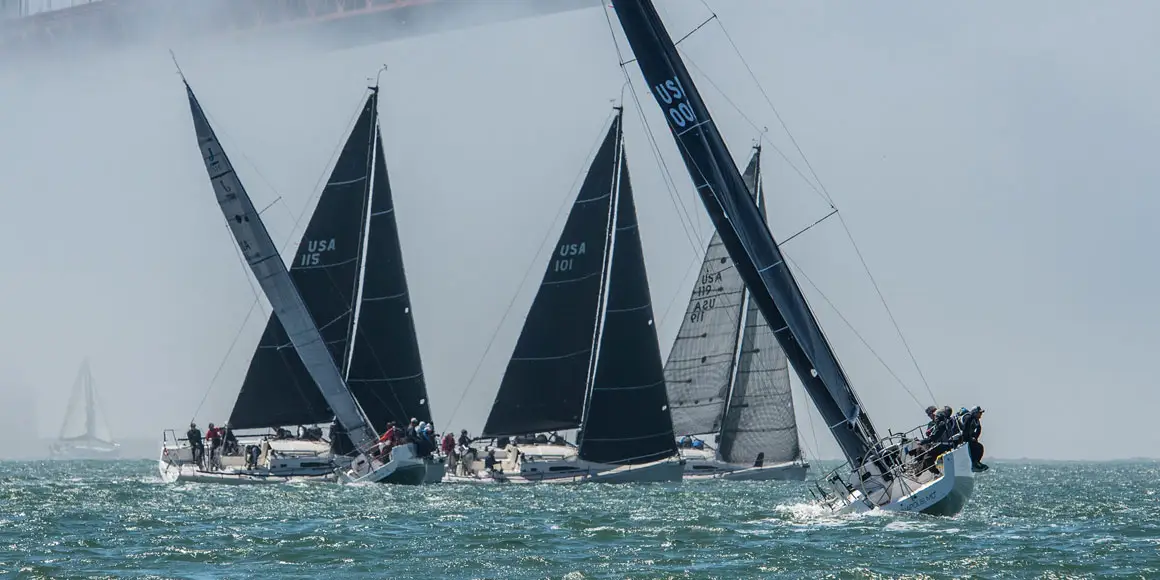 Five J-Boat J/111 sailboats with large black sails in open water during a race.