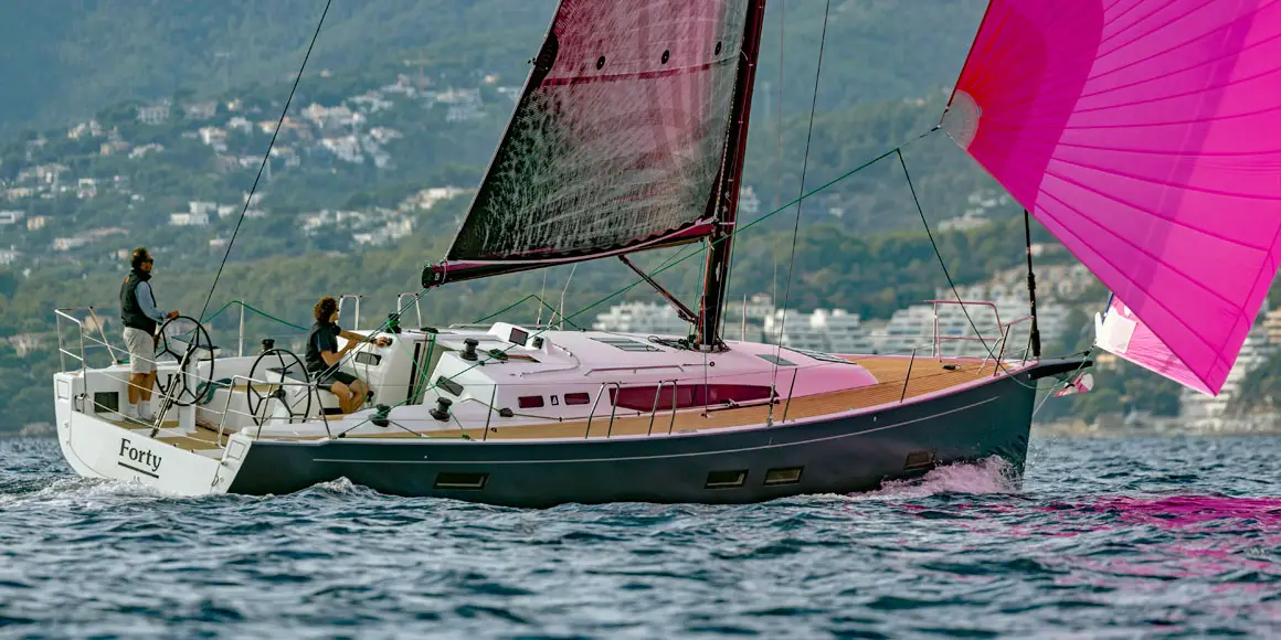 Two people sailing a J-Boat J-40 sailboat with a bright pink sail.