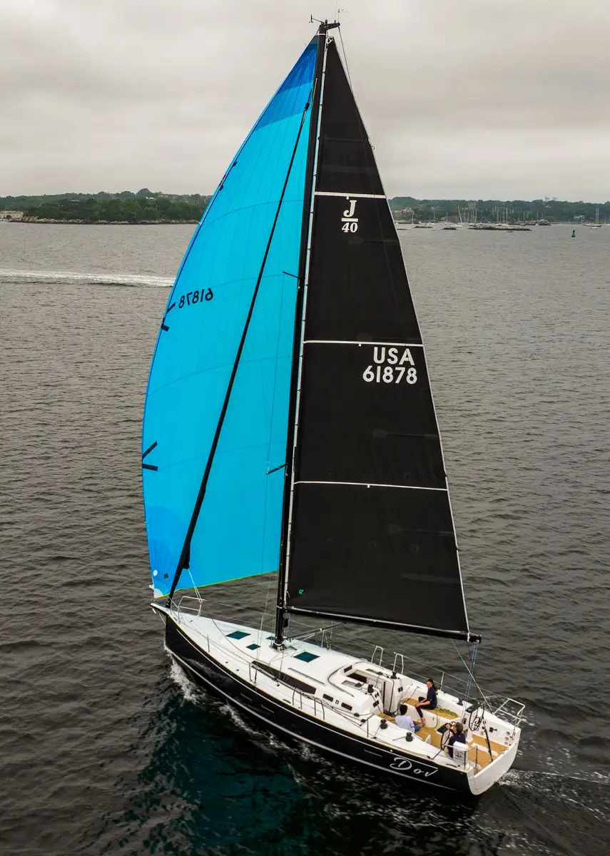 Full view of a J-Boat J-40 sailboat with three sailors and black and bright blue sails.