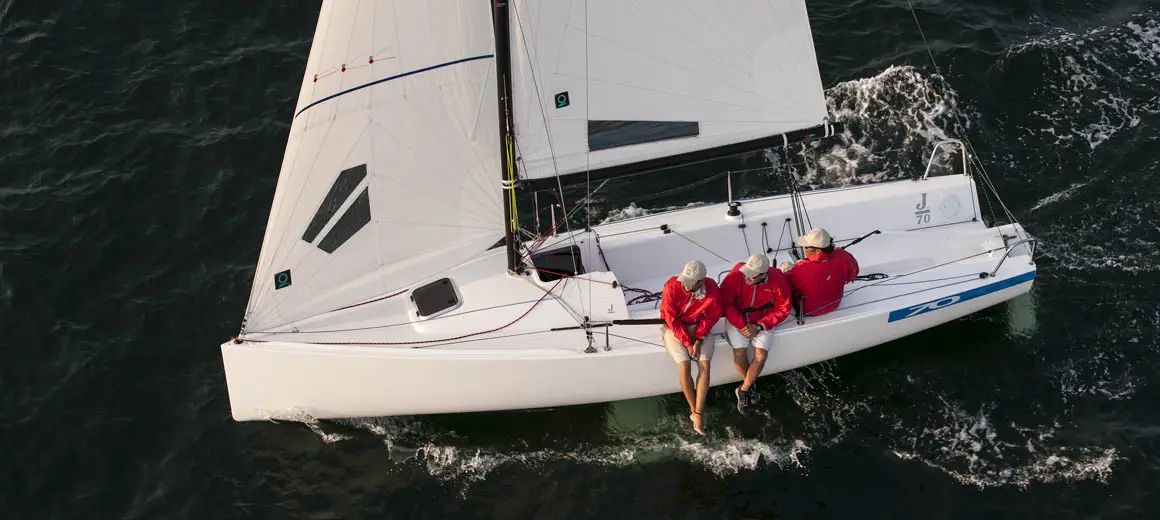Three men in red coats sailing a J-Boat J70 sailboat.