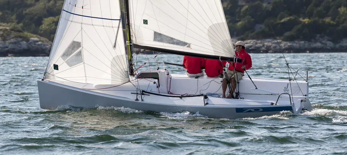 Three men in red coats sailing a J-Boat J70 sailboat.