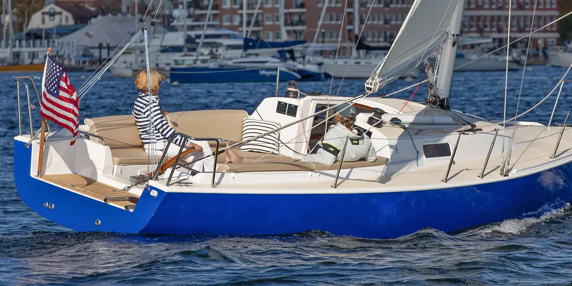Two people lounging in a J-Boat J/9 sailboat near a harbor.