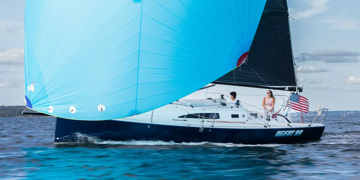 A young couple on Agent 99, a J-Boat J99 sailboat with a bright blue sail.