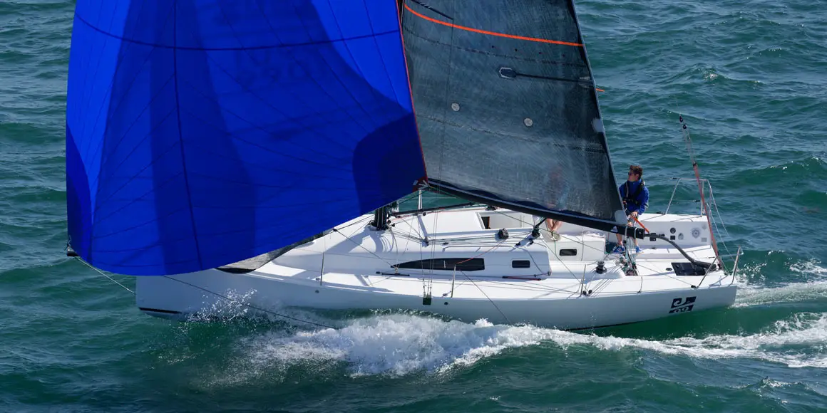 Two person crew sailing a J-Boat J99 sailboat with blue and black sails.
