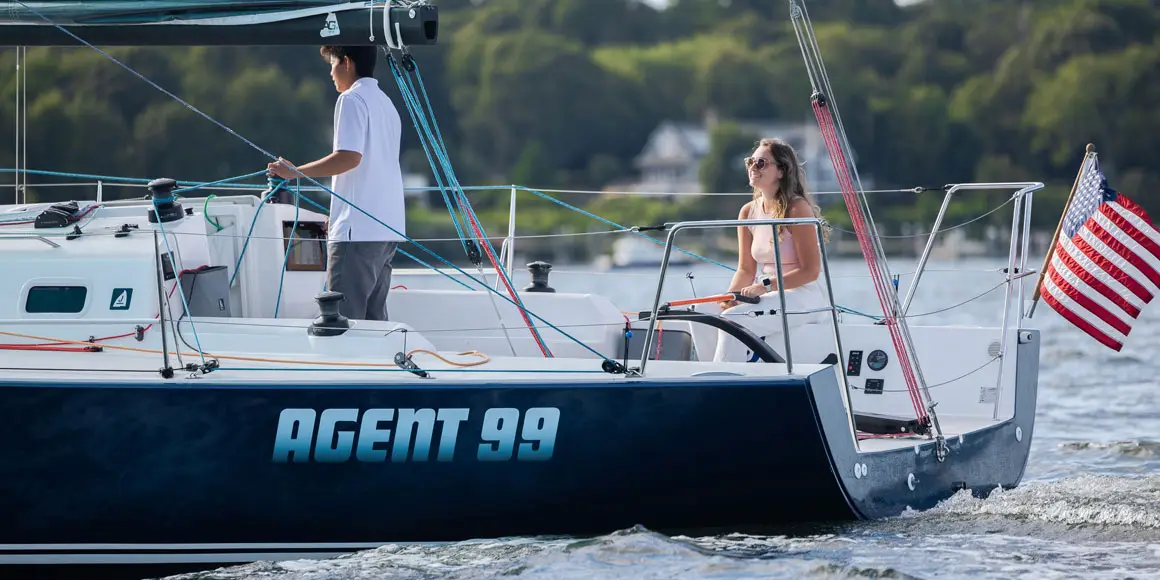 A young couple on Agent 99, a J-Boat J99 sailboat with a bright blue sail.