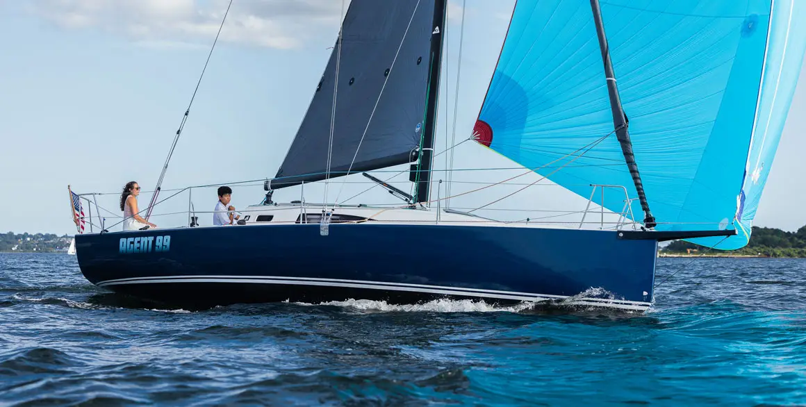 A young couple on Agent 99, a J-Boat J99 sailboat with a bright blue sail.