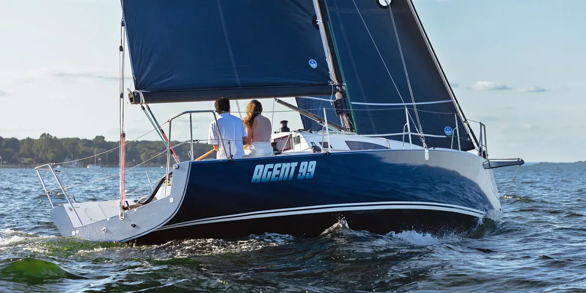 A young couple on Agent 99, a J-Boat J99 sailboat with a bright blue sail.