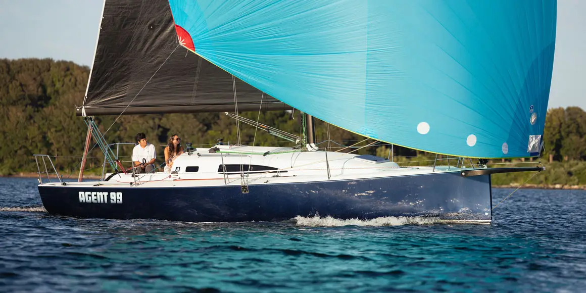 A young couple on Agent 99, a J-Boat J99 sailboat with a bright blue sail.