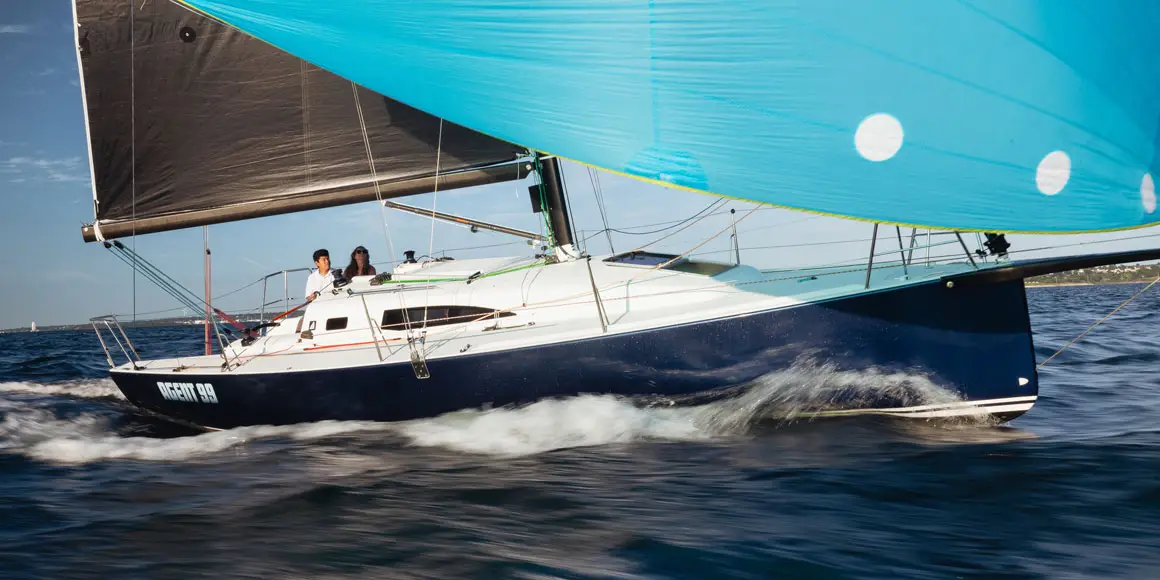 A young couple on Agent 99, a J-Boat J99 sailboat with a bright blue sail.