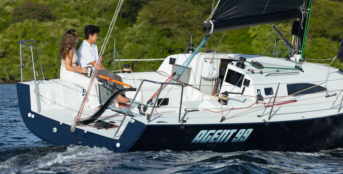 A young couple on Agent 99, a J-Boat J99 sailboat with a bright blue sail.