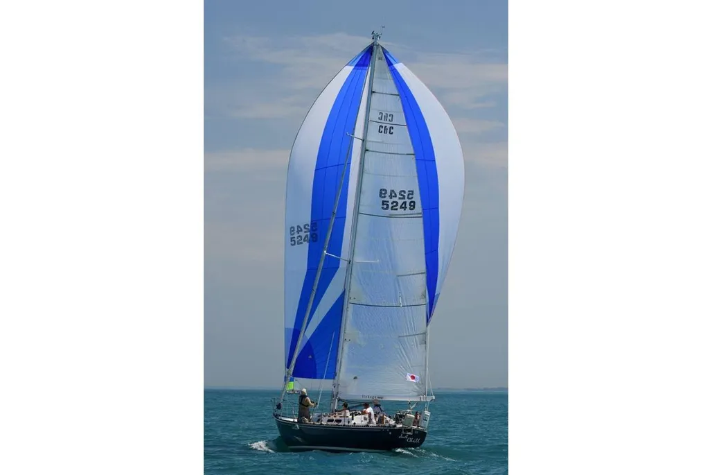 A black-hulled sailboat with a large, fully deployed blue and white striped spinnaker sail races across the deep blue water.