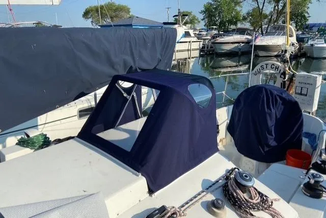 A white sailboat deck featuring a new navy blue canvas dodger and a matching canvas cover over the wheel. Ropes and winches are visible while the boat is docked at a sunny marina.