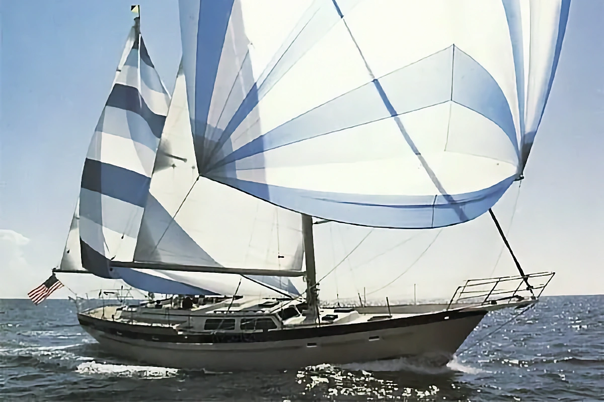 A large sailboat speeds across choppy blue water under a bright sky. The huge white and blue striped sails are fully deployed and catching the wind.