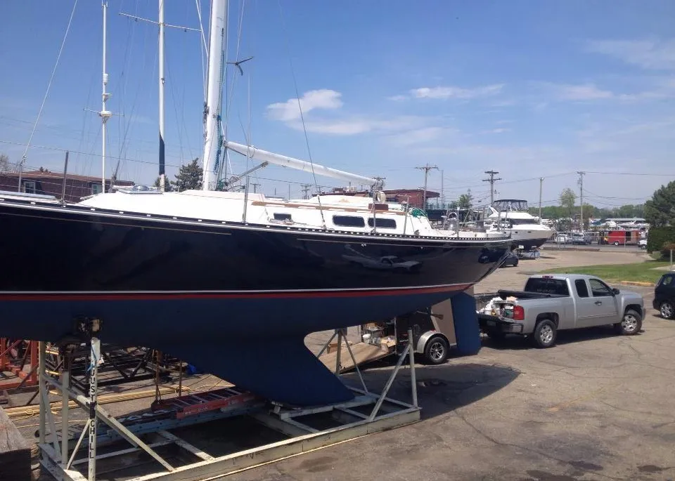 A large, glossy dark blue sailboat is dry-docked on a metal storage cradle under a clear blue sky at Port Sanilac Marina.