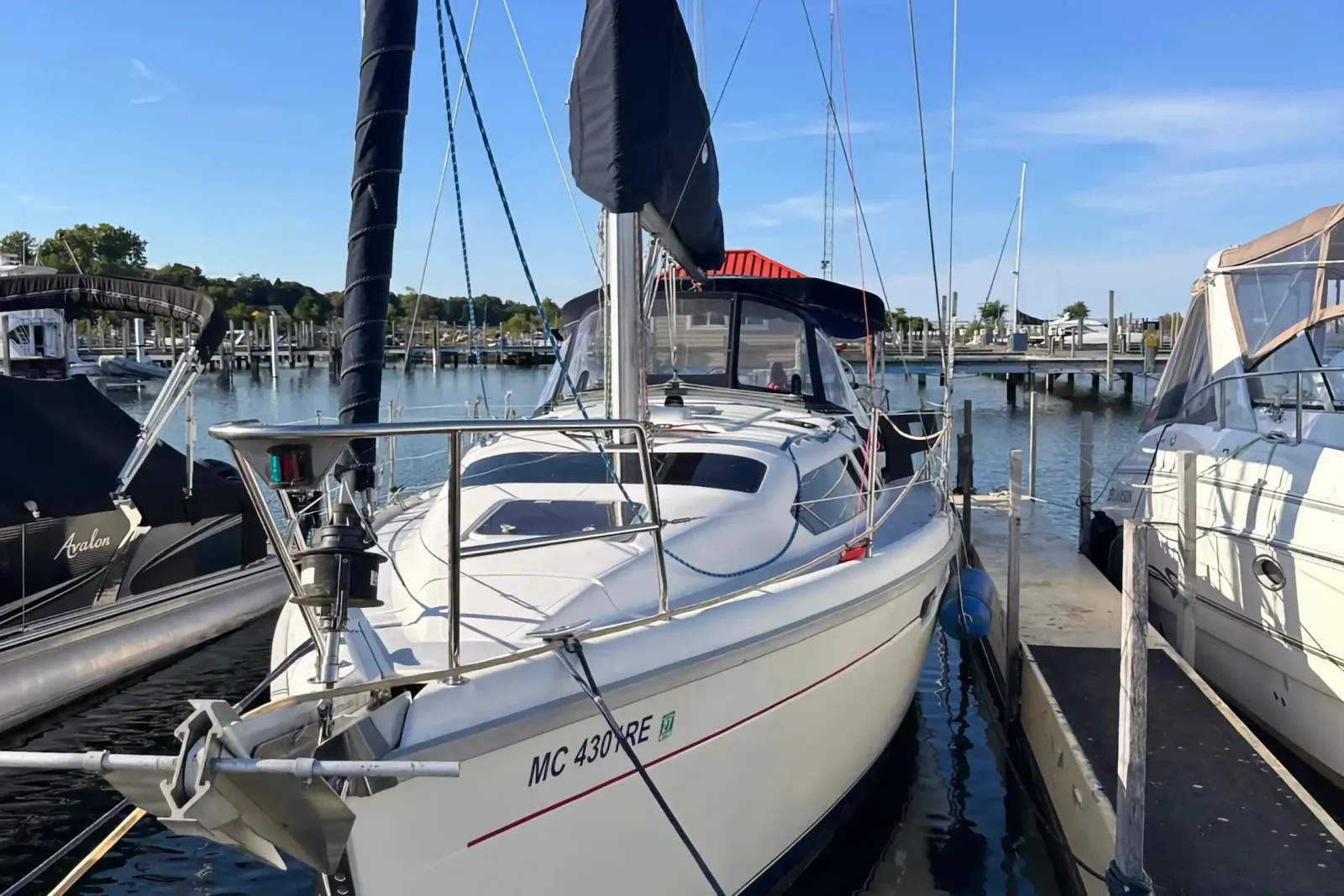 A white sailboat with a dark blue canopy is secured at a wooden marina slip on a bright, sunny day.