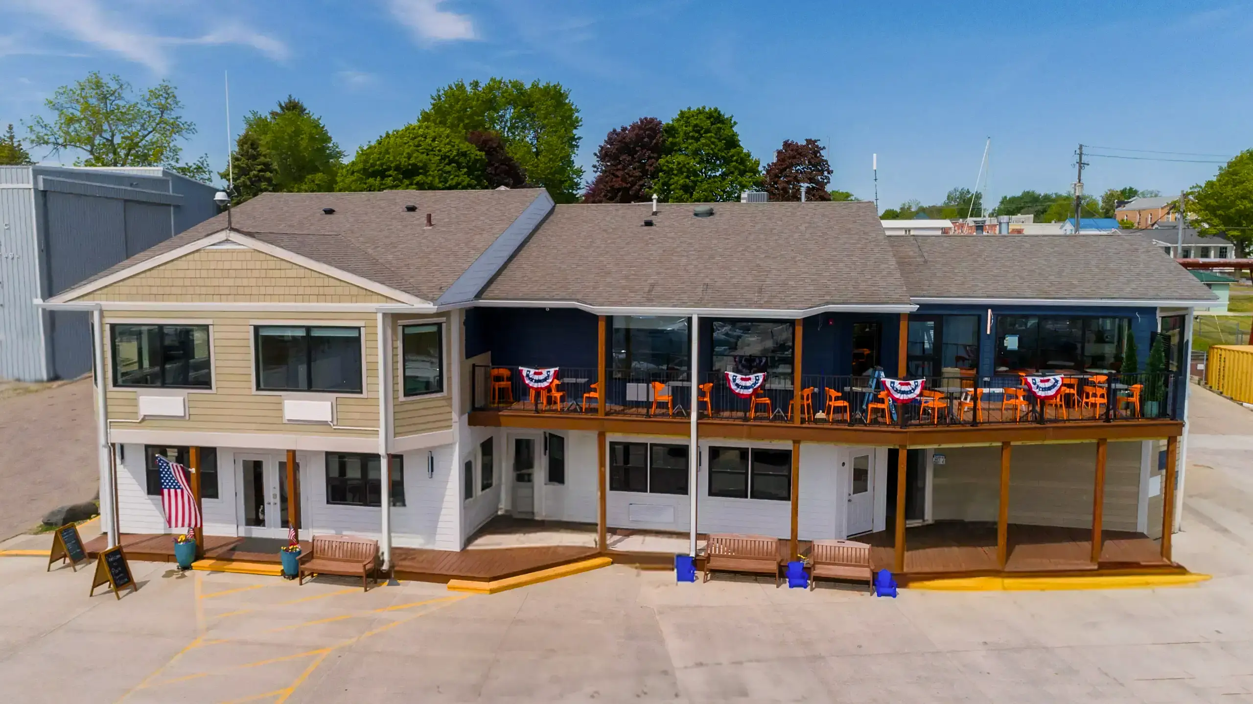 The two-story exterior of the Port Sanilac Marina main building, which features tan and dark blue siding. A balcony holds orange chairs and patriotic bunting.