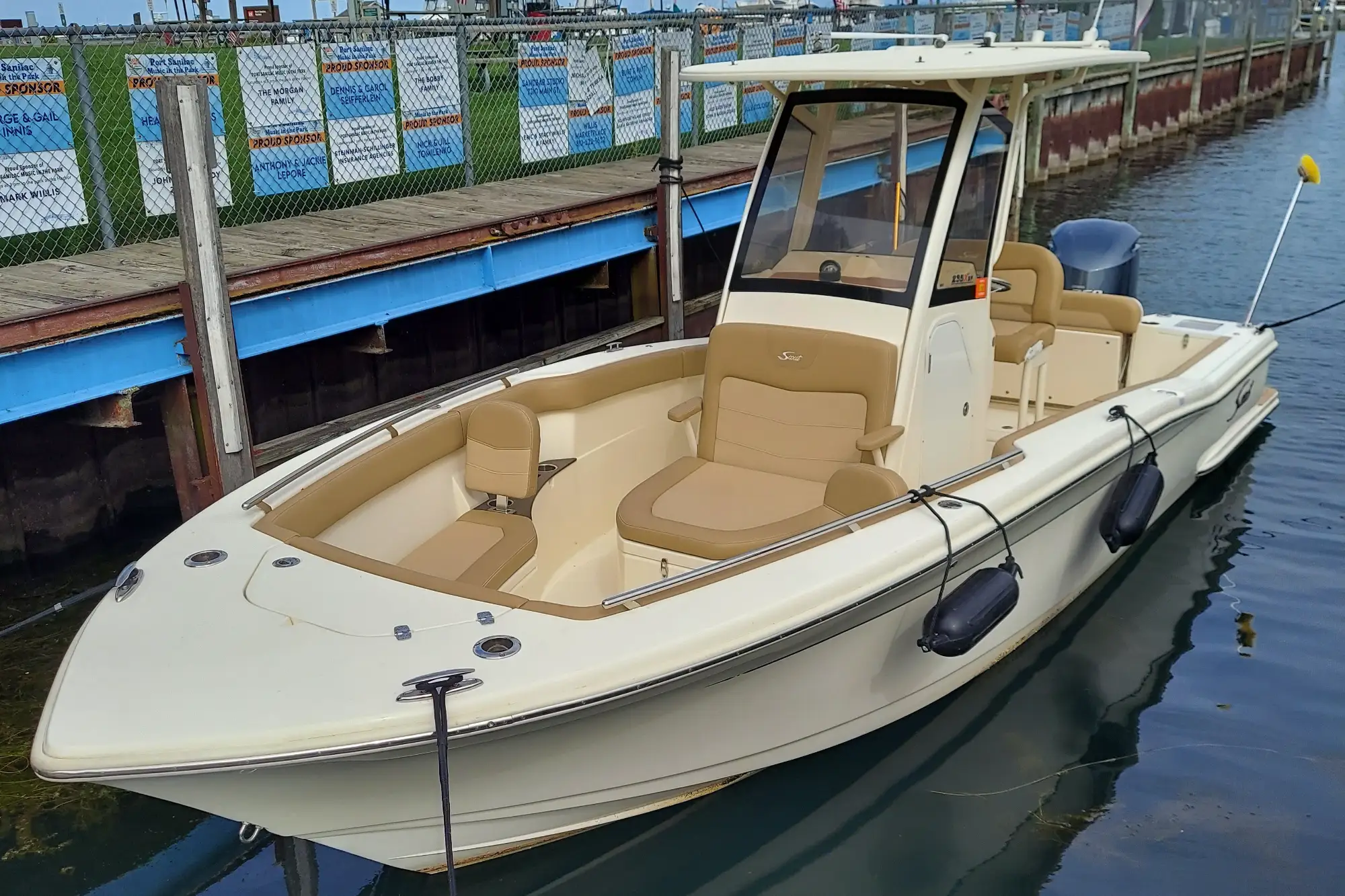 A white Scout 235 center console sport fishing boat with tan upholstery is securely tied to a wooden dock at a marina.